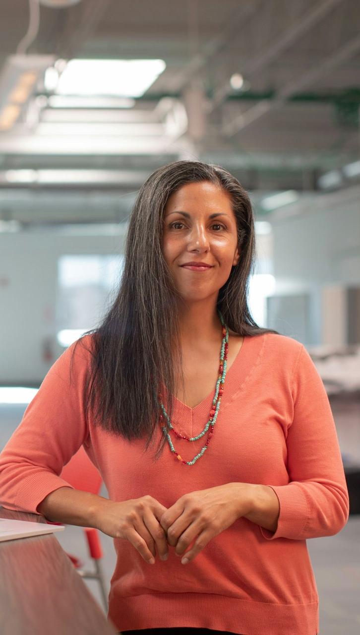 woman in orange long sleeve shirt sitting beside table with macbook pro